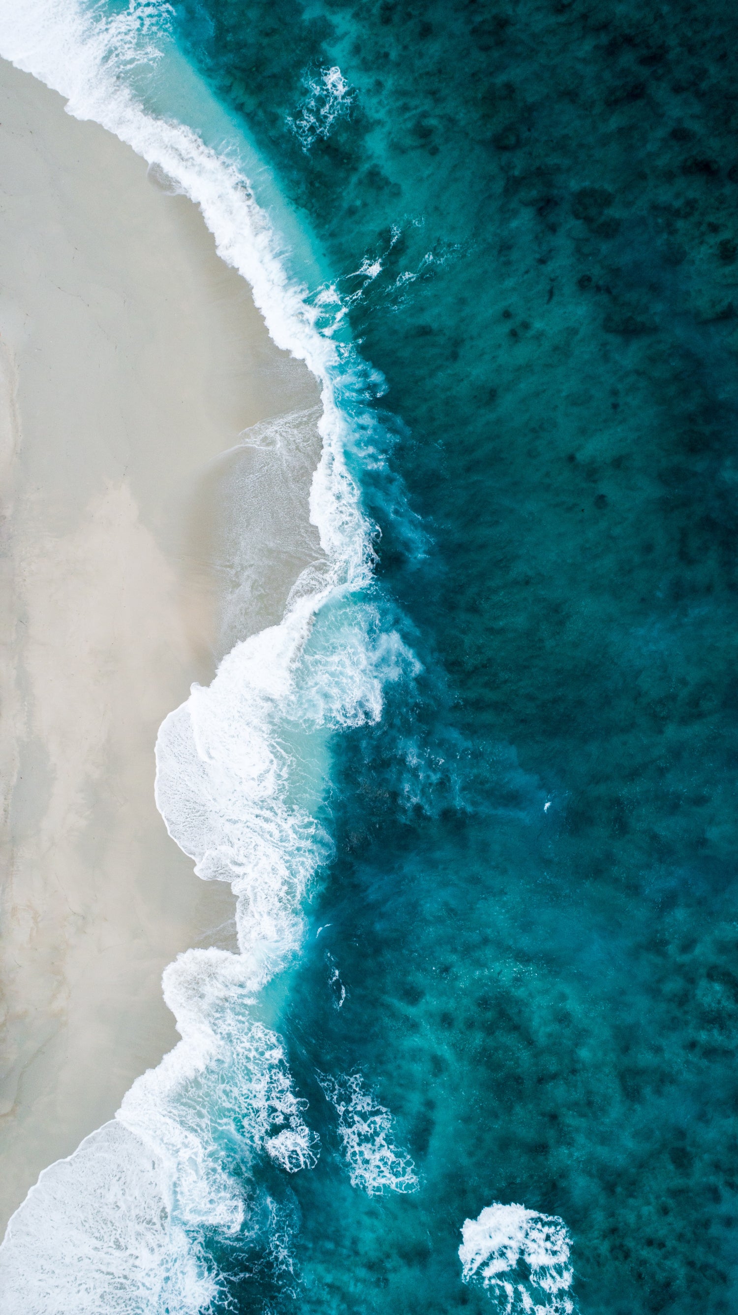 Bovenaanzicht van diepblauwe oceaan en wit strand